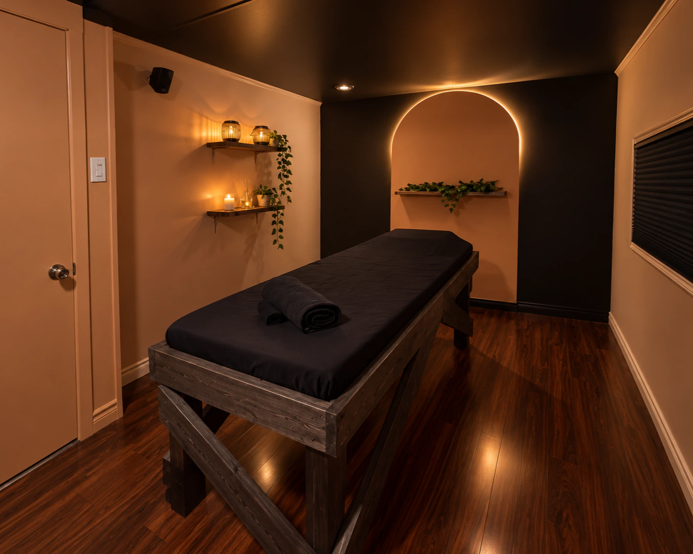 La salle Sakura&nbsp;: murs beige rosé, arche rétroéclairée garnie de plantes, chandelles sur tablettes et table de massage en bois foncé